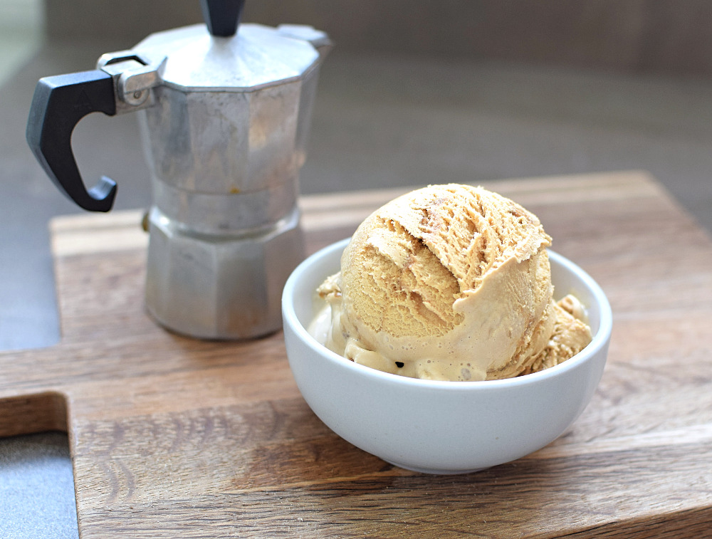 A bowl of coffee ice cream with a jug of coffee next to it.