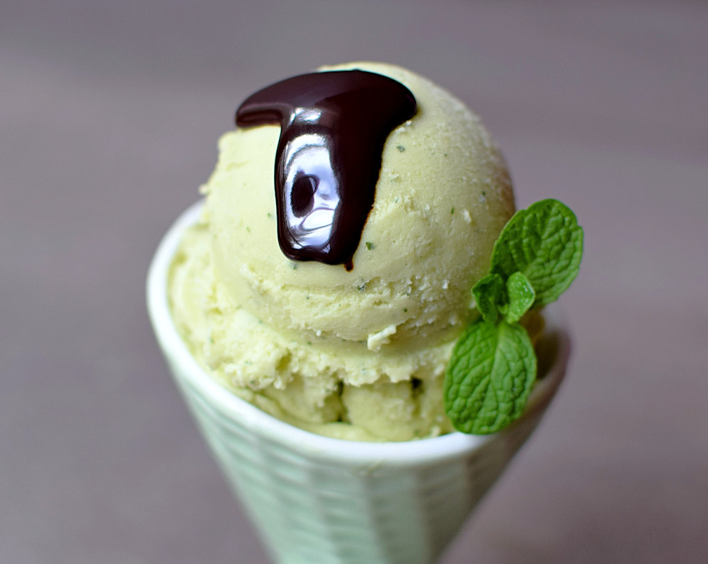 A bowl of avocado ice cream topped with chocolate sauce and a mint garnish.