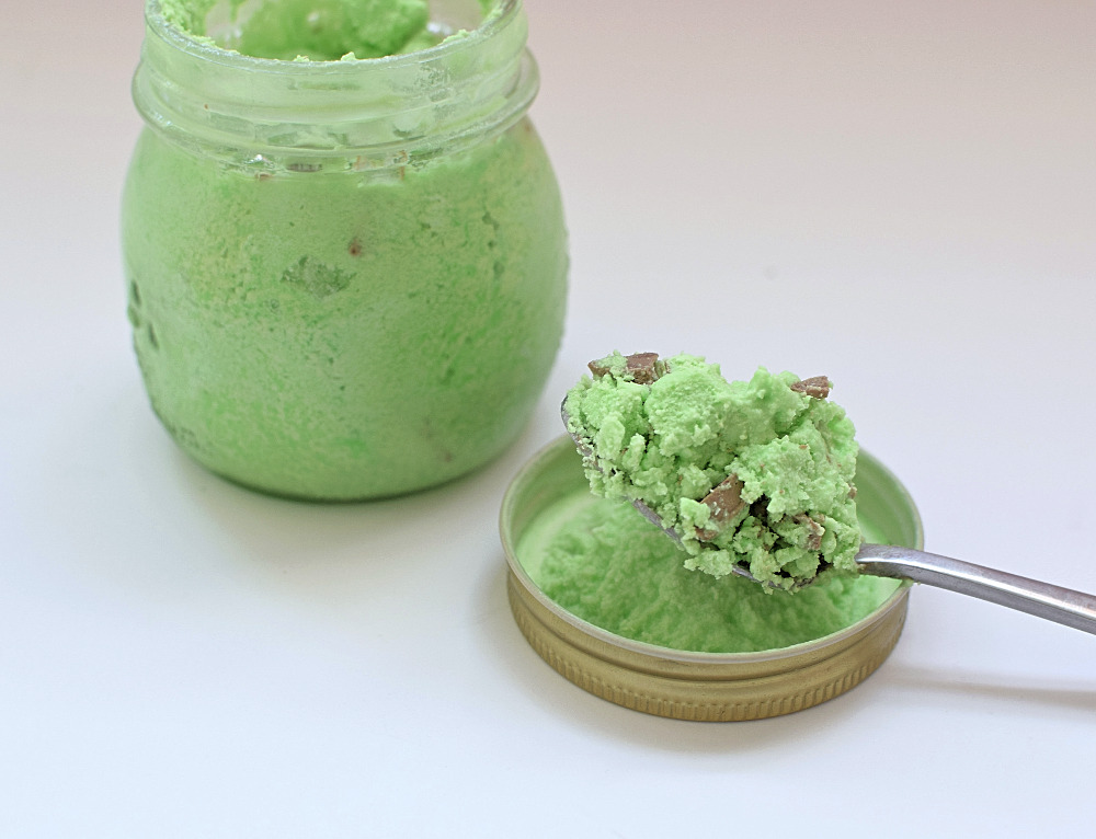 A jar of mint choc chip ice cream and a spoon of ice cream next to it.