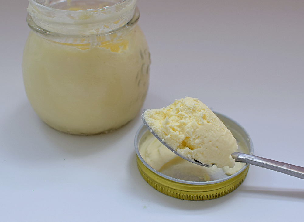 A jar of vanilla ice cream next to a spoon of ice cream.