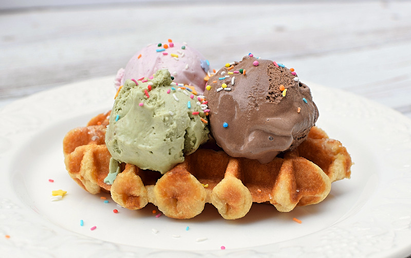 Scoops of chocolate, strawberry and pistachio ice cream on a waffle.