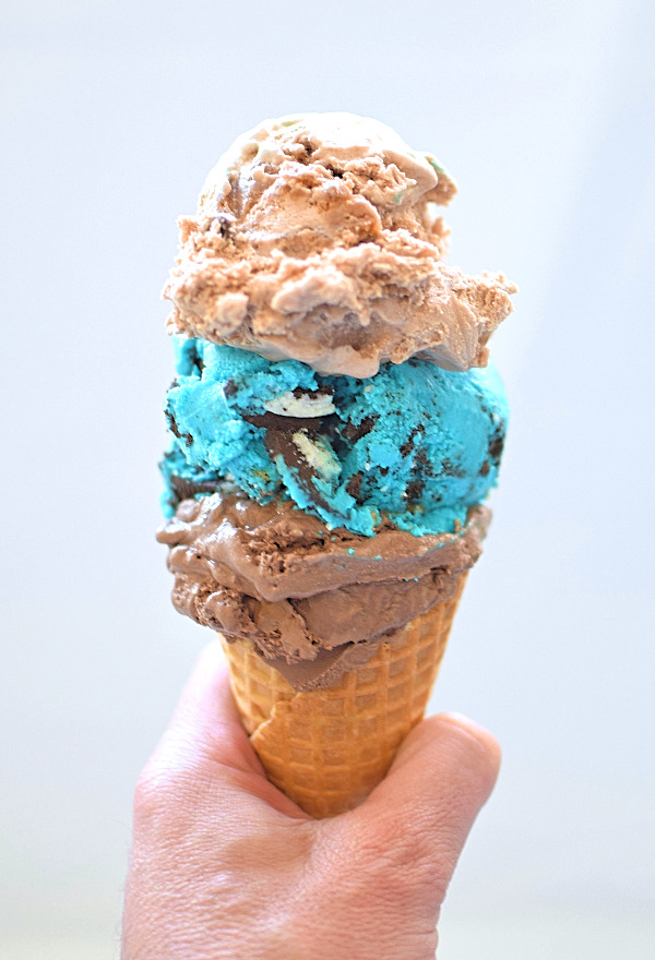 Waffle cone with scoops of chocolate, cookie monster and blondie ice cream.