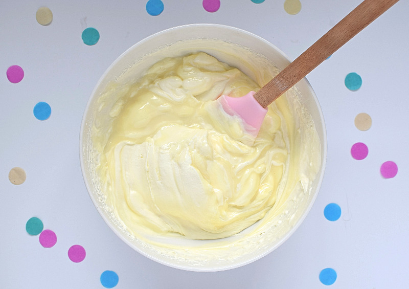 A bowl of cream, condensed milk and a spatula.