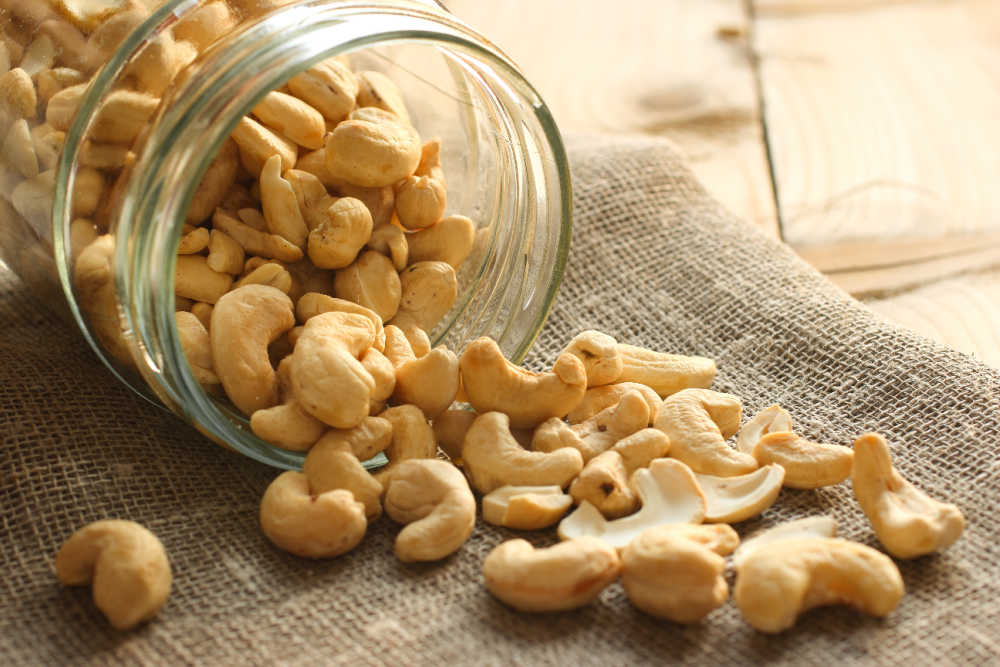 Cashews spilling out of a glass jar onto a burlap sack.