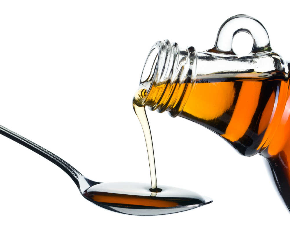 Pouring maple syrup into a spoon on white background.