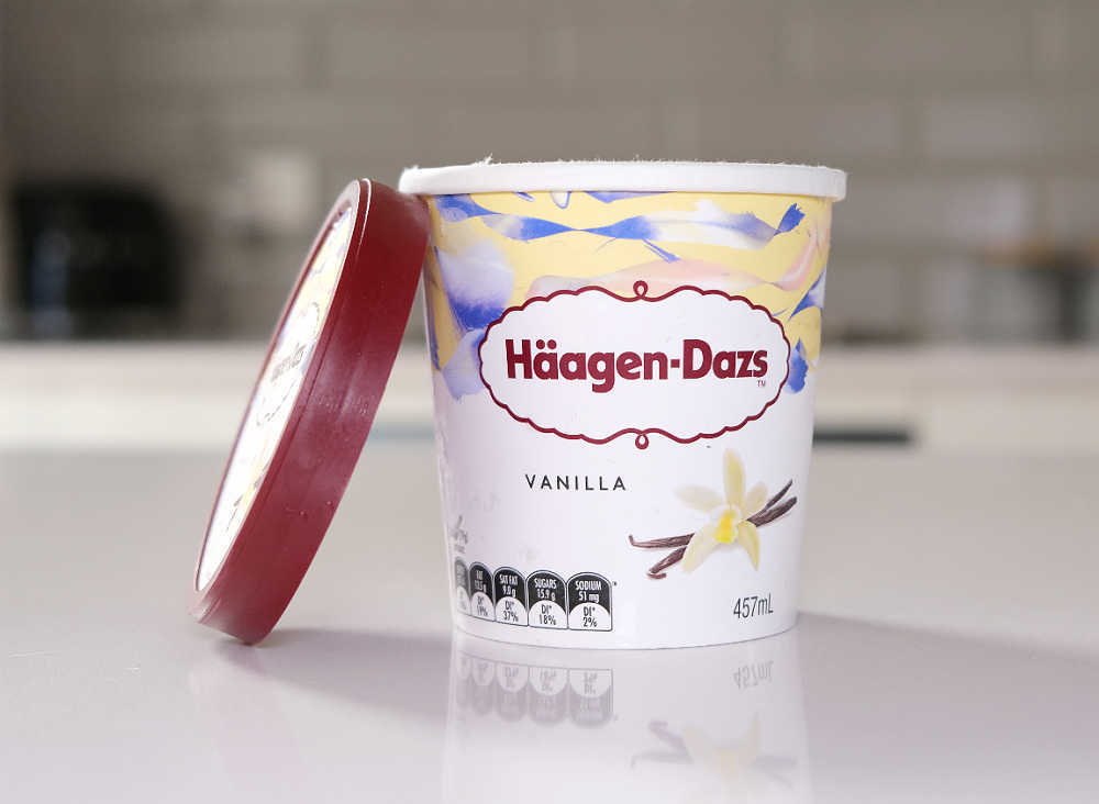 A shot of an open container of Haagen-Dazs Vanilla with the lid leaning against the side.