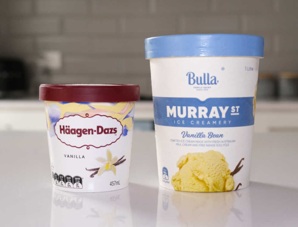 A tub of Haagen-Dazs next to a tub of Murray St on a bench. Both are vanilla flavour.