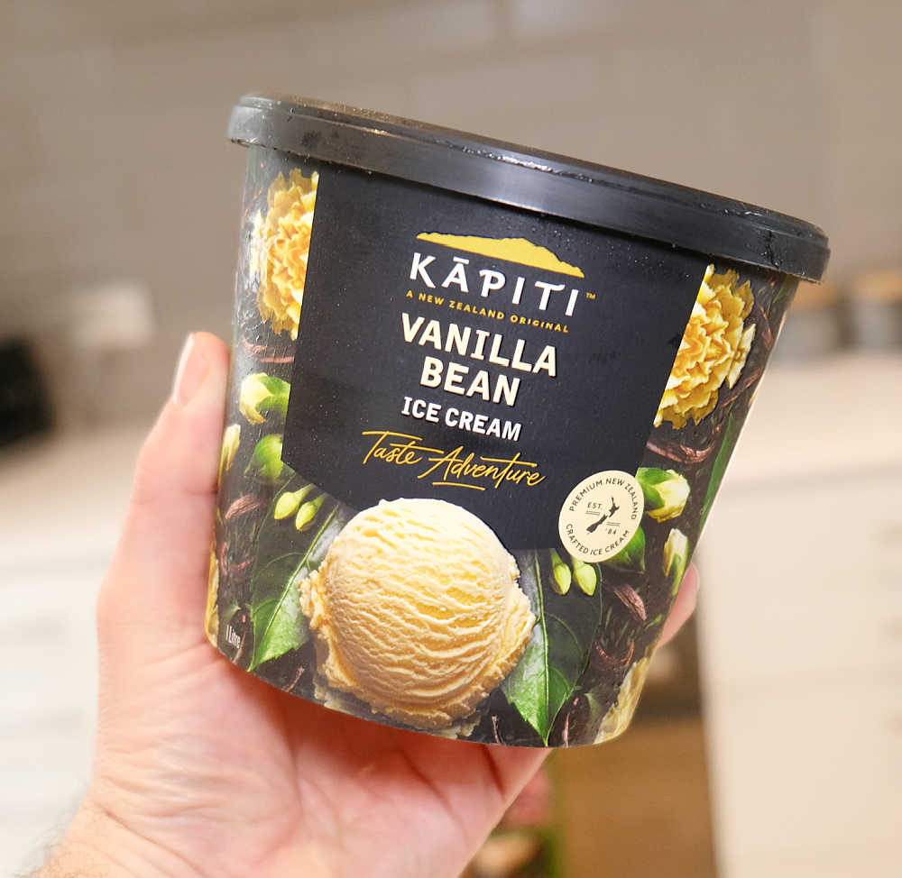 A hand holding a one-litre container of Kapiti Vanilla Ice Cream.