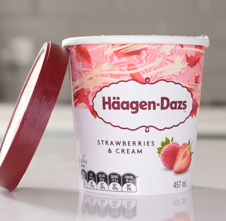 A front on shot of a 457ml tub of Haagen-Dazs Strawberries Cream Ice Cream with the lid leaning against the side.