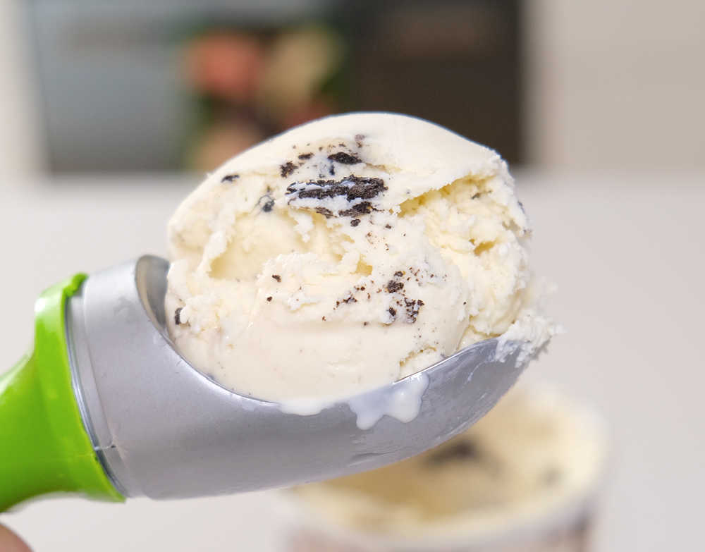 An ice cream scoop full of cookies and cream ice cream with a blurred kitchen in the background.