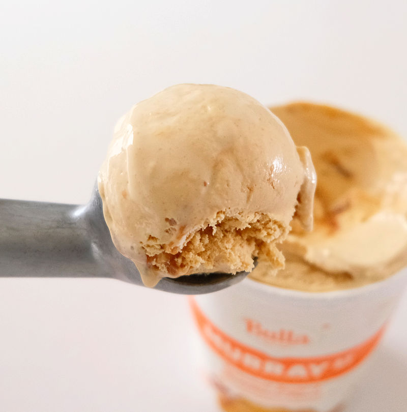 Close up photograph of a scoop of Caramel Swirl Ice Cream with the tub in the background.