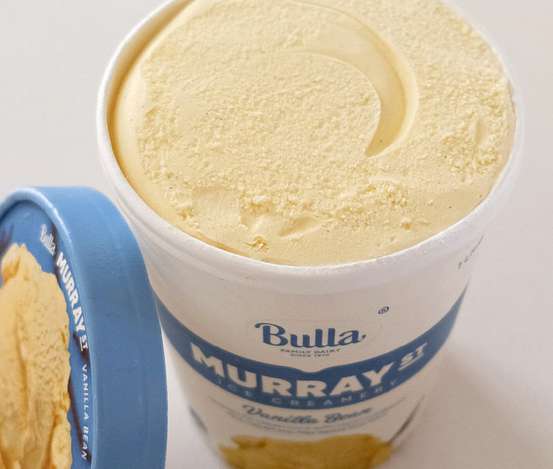 The lid leaning against an opened tub of vanilla bean ice cream