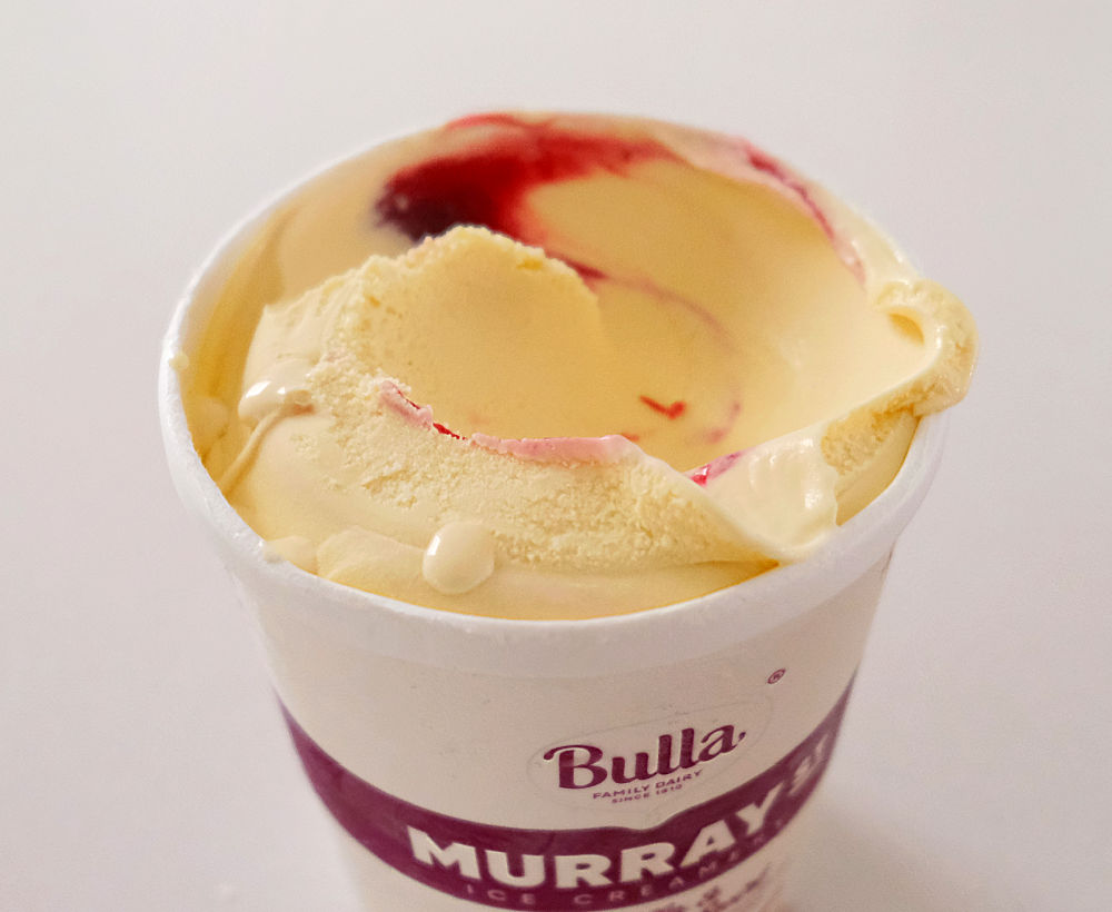 A tub of Murray St Vanilla and Boysenberry ice cream with a scoop missing.