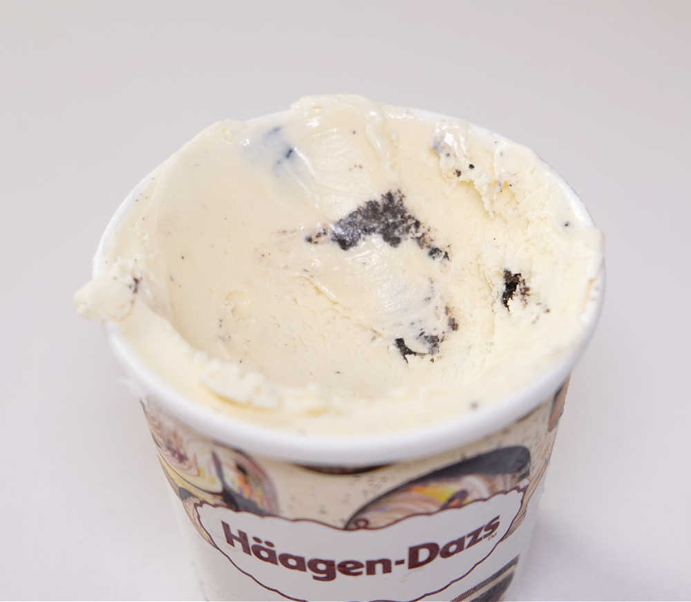 A partially scooped tub of Haagen-Dazes Cookies and Cream Ice Cream isolated.