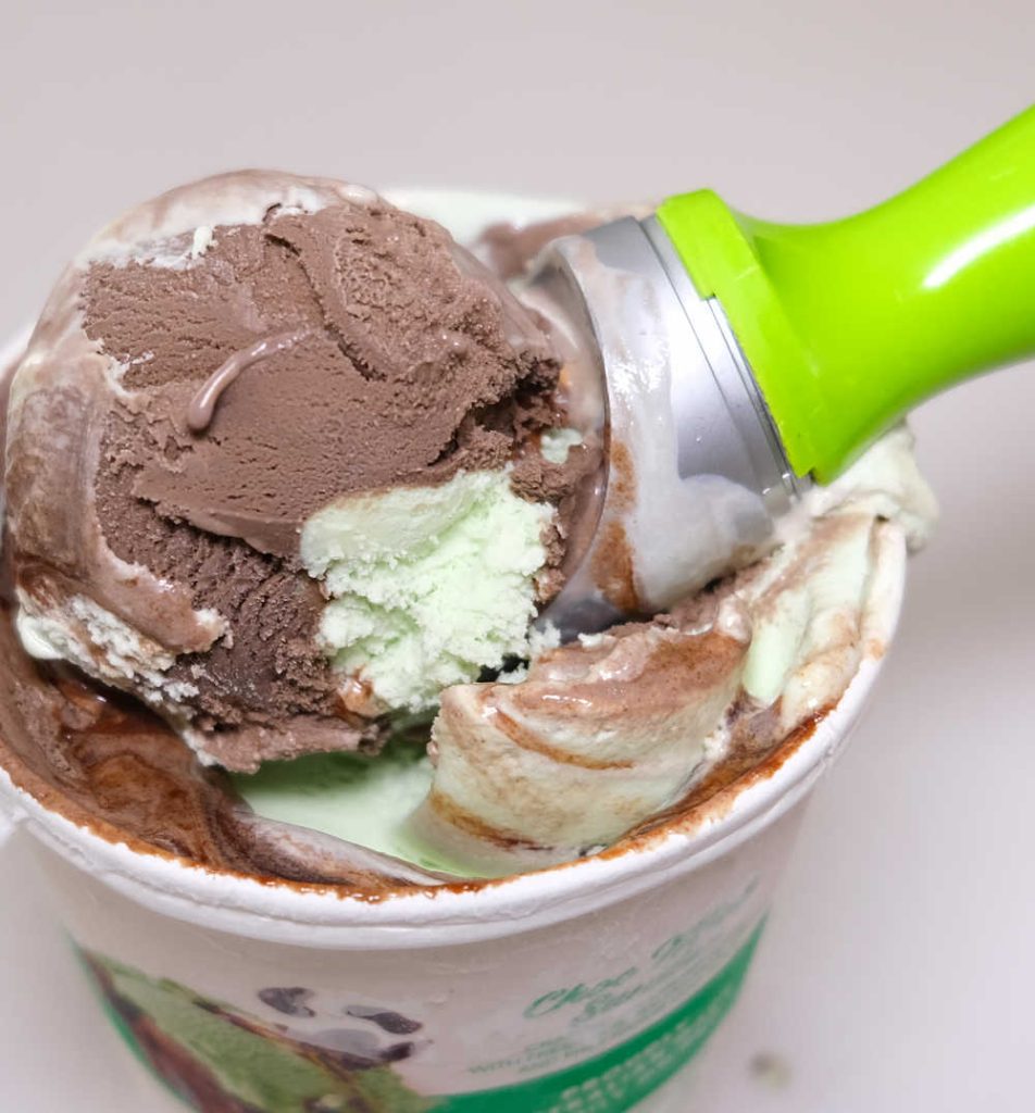Zoomed in image of a large scoop of choc mint sundae ice cream resting on the opened tub.