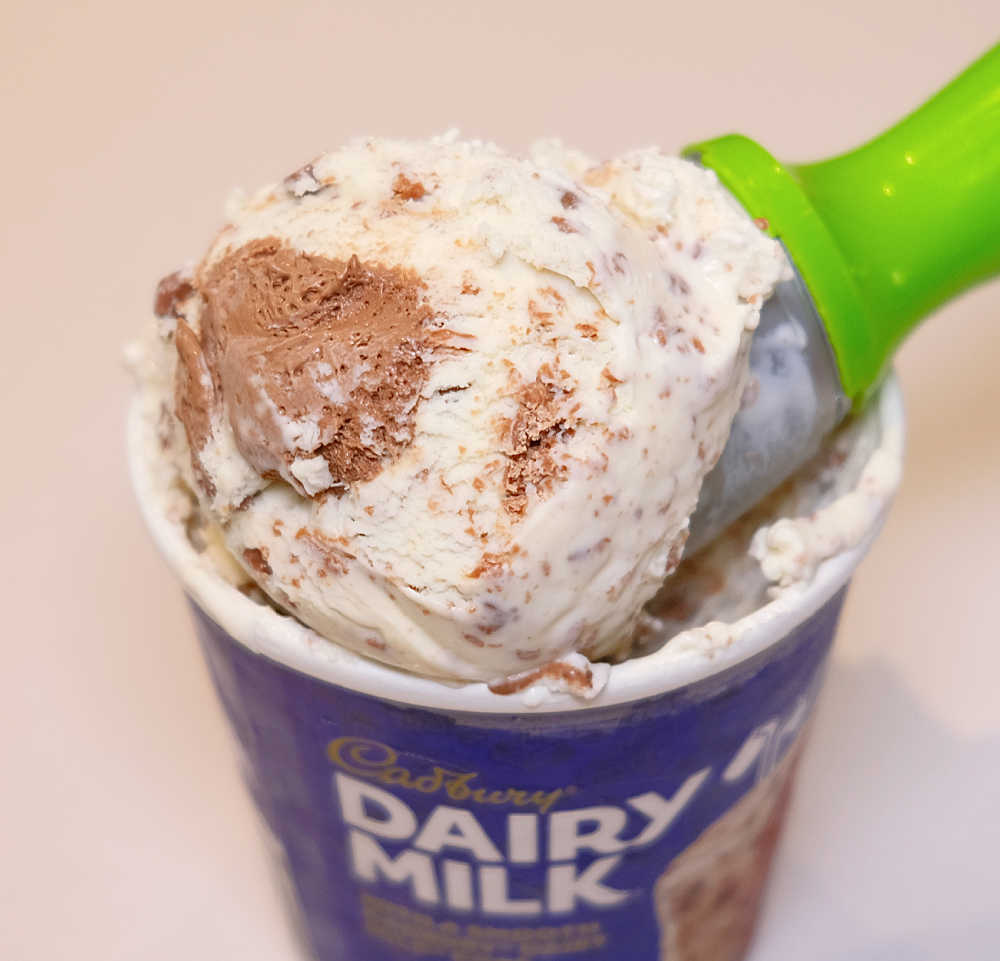 An ice cream scoop full of Cadbury Dairy Milk resting on the container.