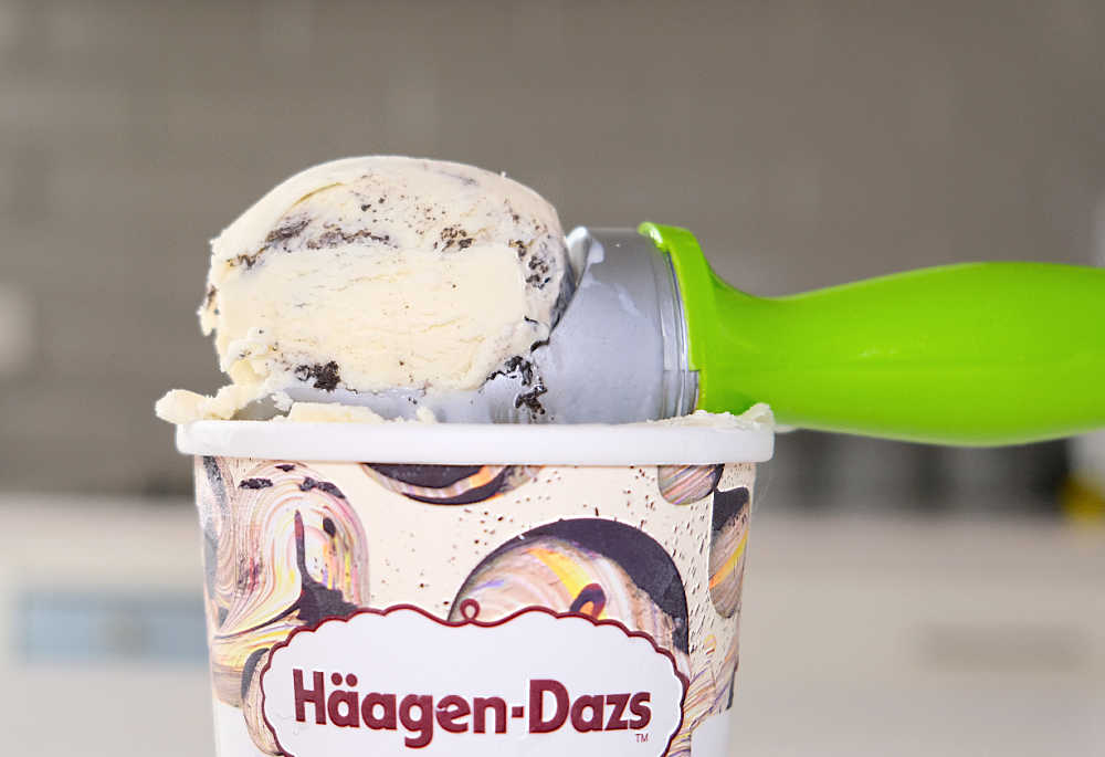 A scoop of cookies and cream ice cream resting on a Haagen-Dazs tub.