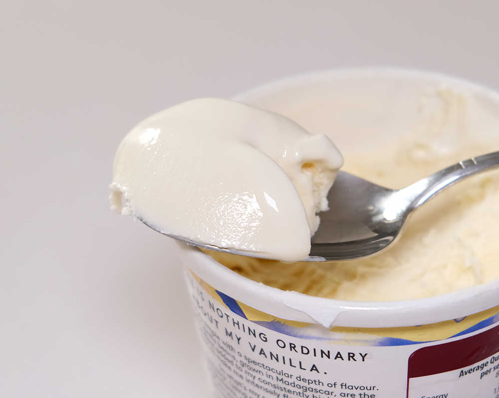 A spoon of ice cream resting against the Haagen-Dazs tub.