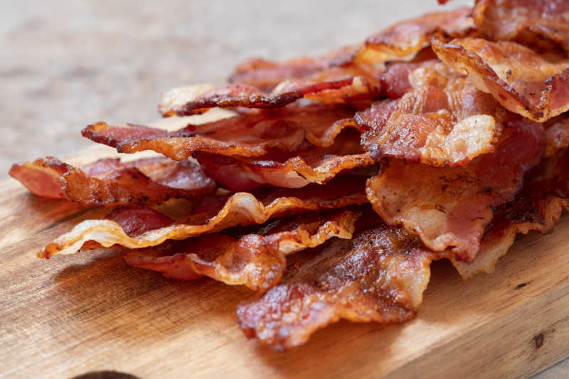 Cooked streaky bacon on a chopping board.