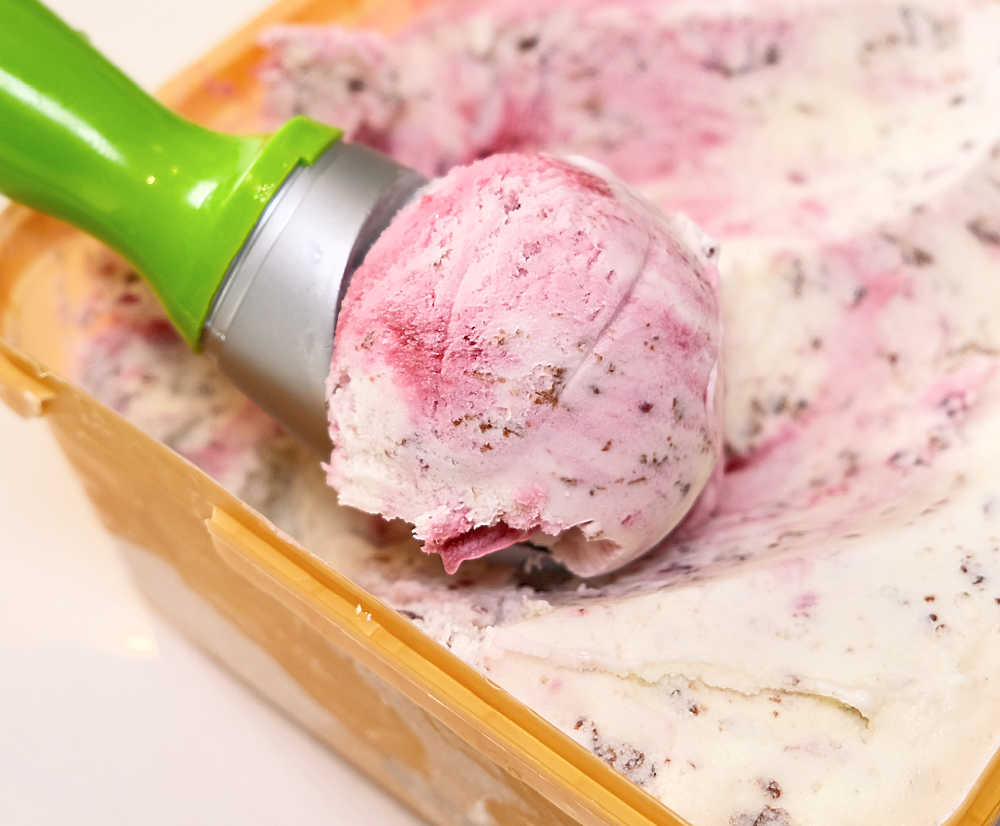 A scoop of Much Moore Awesome Boysenberry Stracciatella ICe Cream leaning on the top of the tub.
