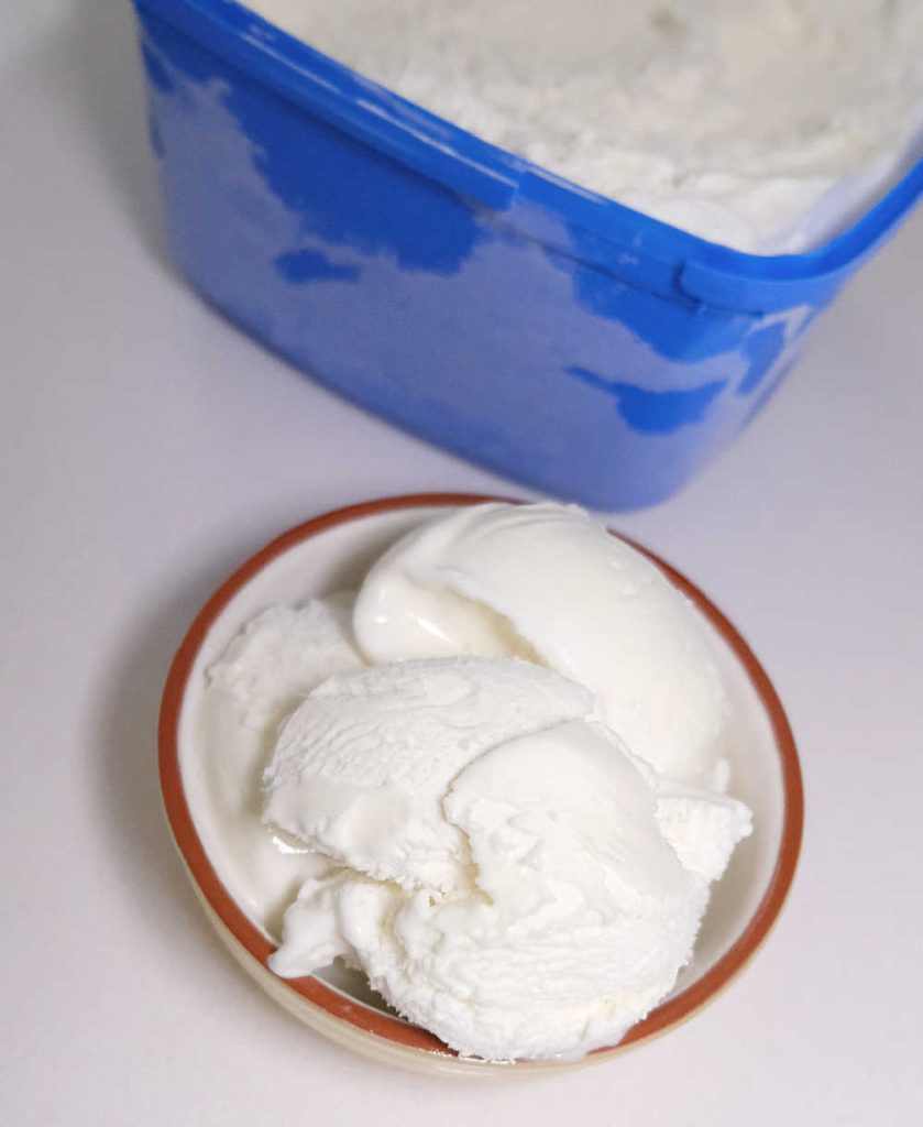 A top down photo of a bowl of Peters Vanilla ice cream next to the tub.