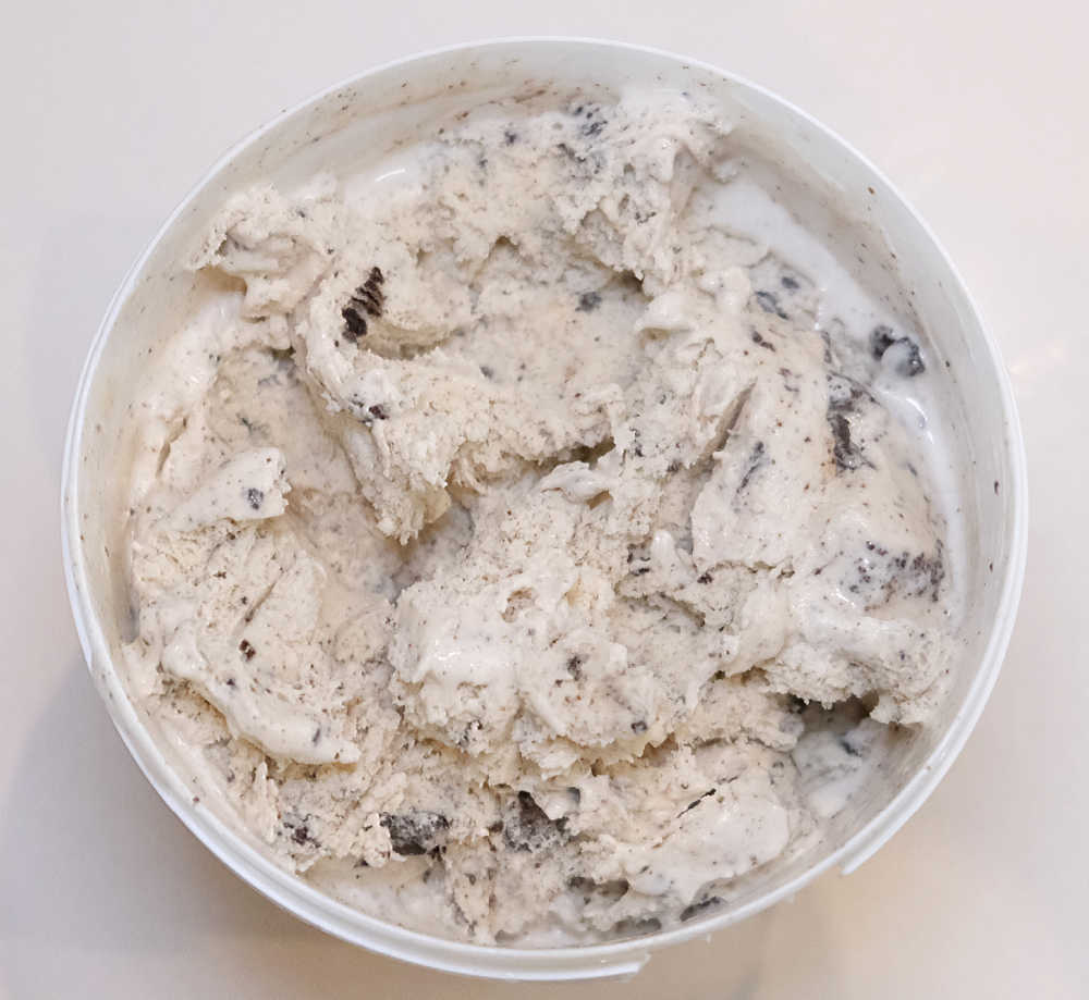 Top-down photo of an partly eaten container of Woolworths Cookies Cream 1L.