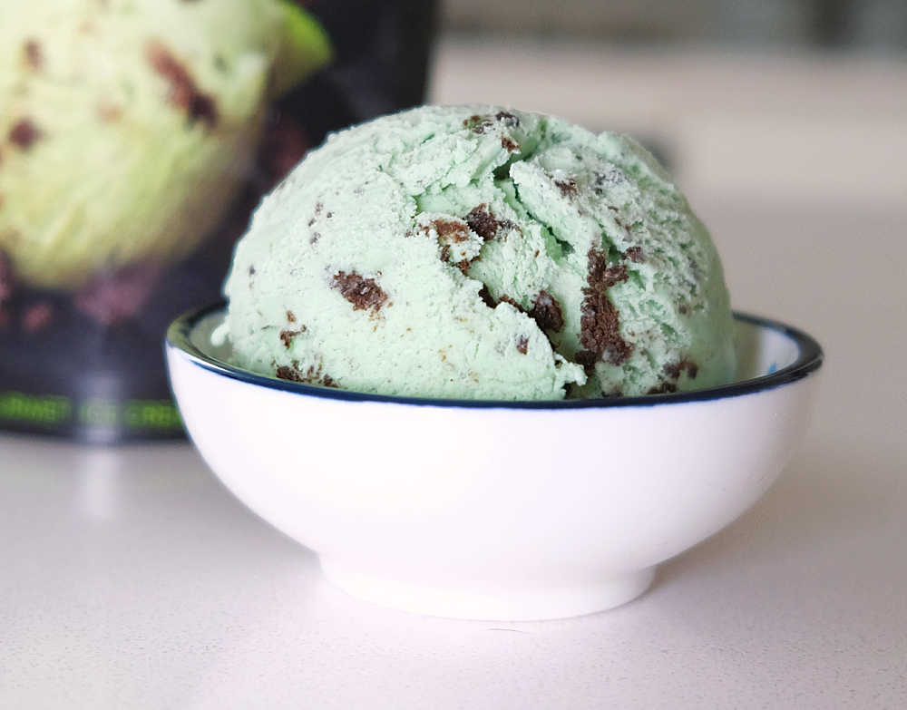 A bowl of Mint and Cookies Ice Cream with the tub in the background.