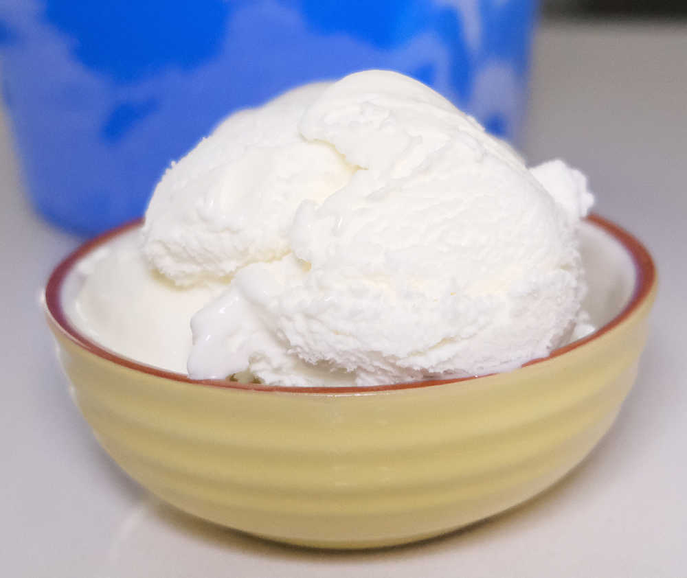 A bowl containing scoops of vanilla ice cream by Peters with the blue pack in the background.