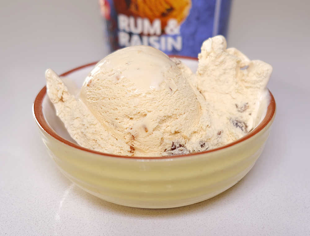 A bowl full of Coles Rum and Raisin Ice Cream with the tub in the background.