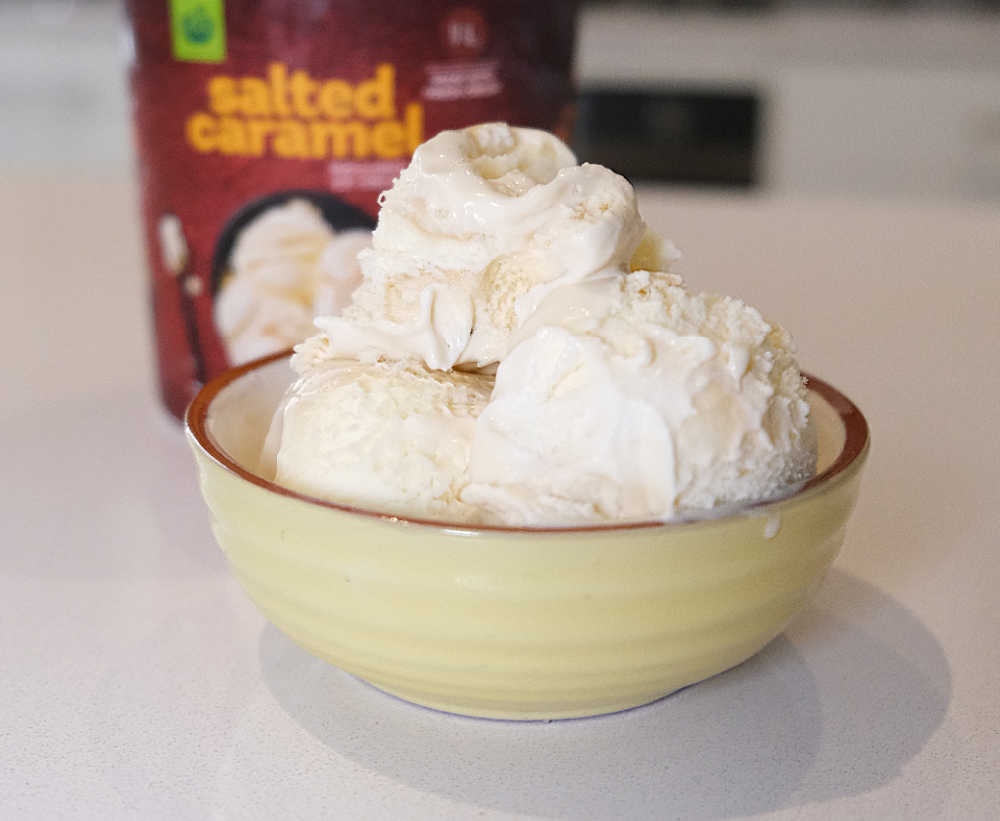 A bowl with scoops of salted caramel ice cream and the container in the background.