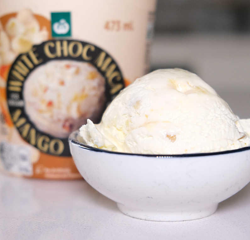 A bowl of Woolworths White Chocolate Maca Mango Ripple Ice Cream with pack in the background.