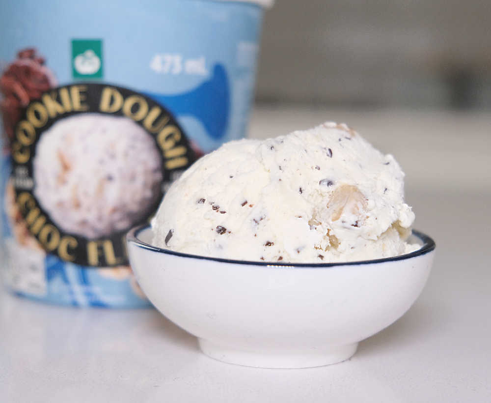 A bowl of Cookie Dough Choc Flakes Ice Cream with a tub in the background.