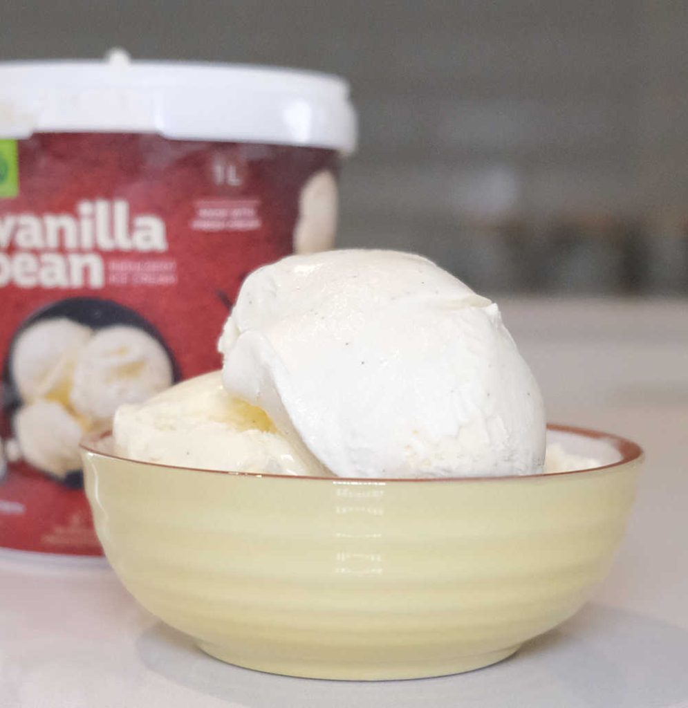 A bowl filled with scoops of vanilla bean ice cream with the container in the background.