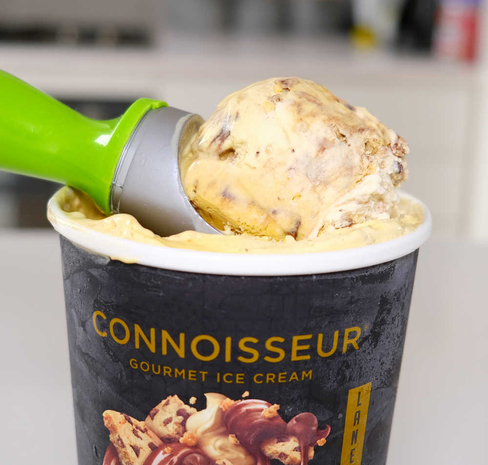 A scoop of Connoisseur Choc Chip Cookie Ice Cream resting on a tub.