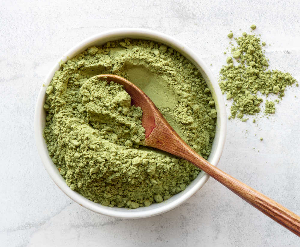 A top-down photo of matcha powder in a small bowl with a wooden spoon.