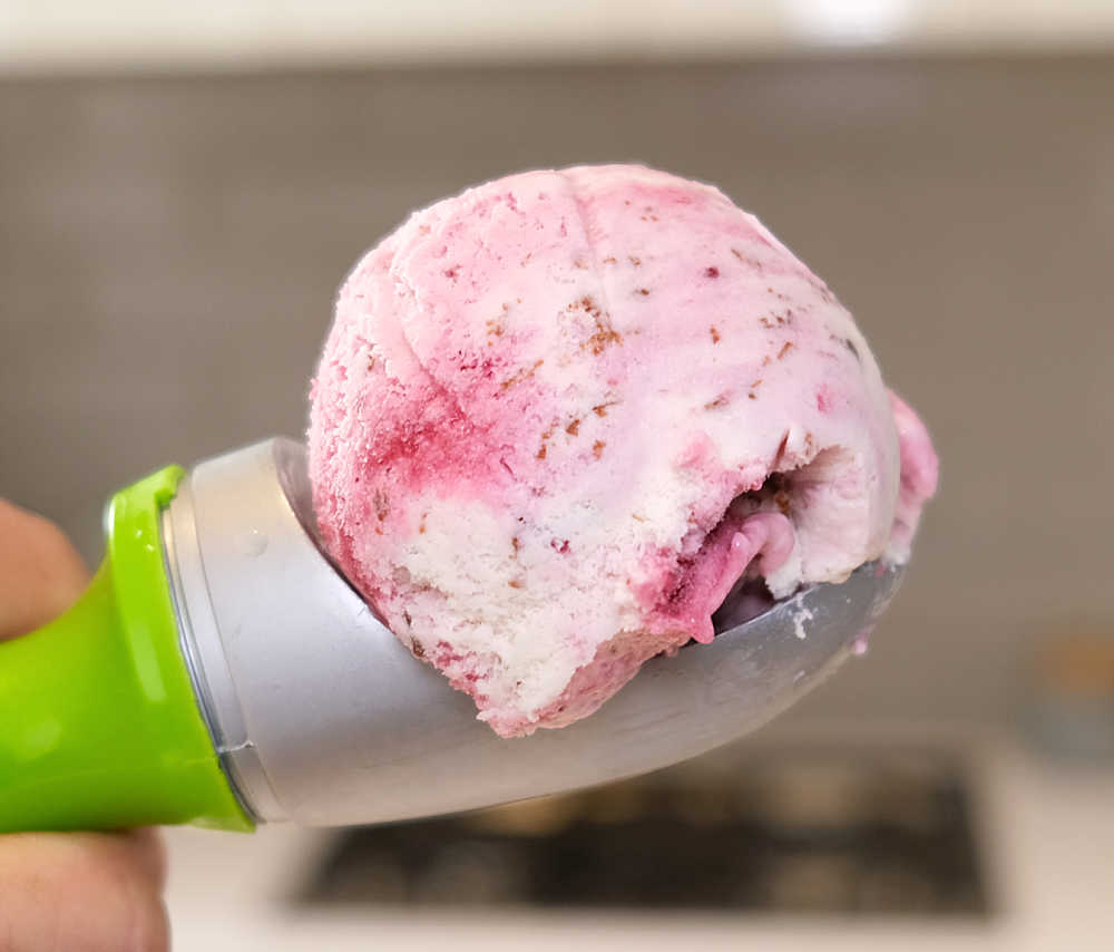 A macro of a scoop of Boysenberry Stracciatella with a blurry kitchen background.