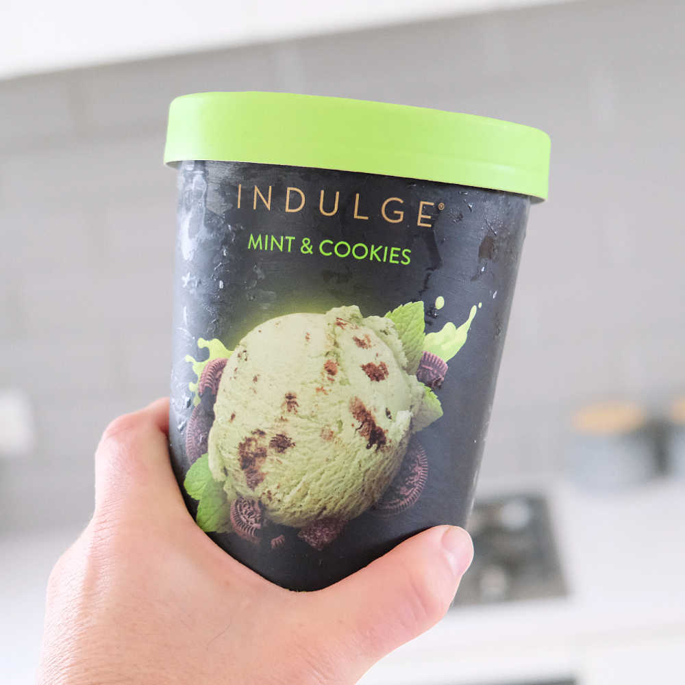 A hand holding a container of Indulge Mint and Cookies Ice Cream.