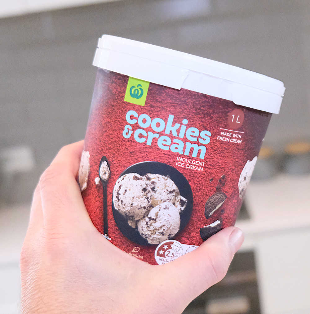 A hand holding a tub of cookies and cream ice cream.