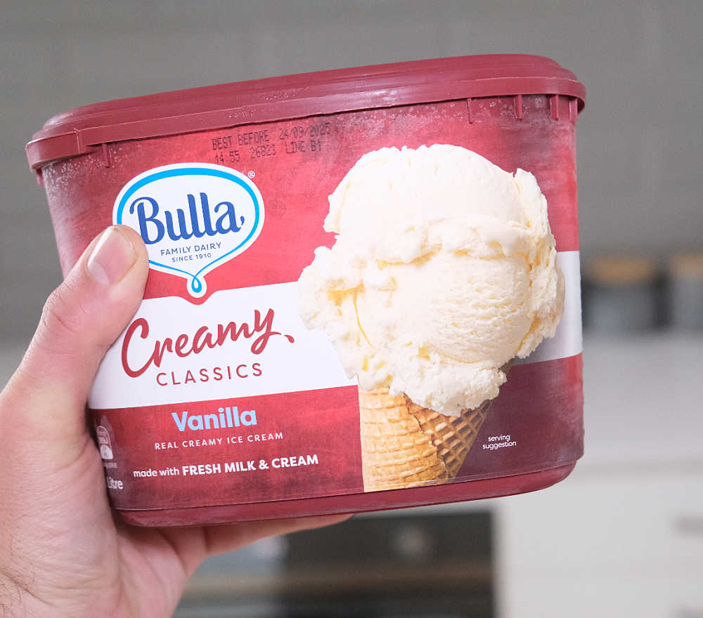 Holding a 2L pack of Creamy Classics Vanilla.