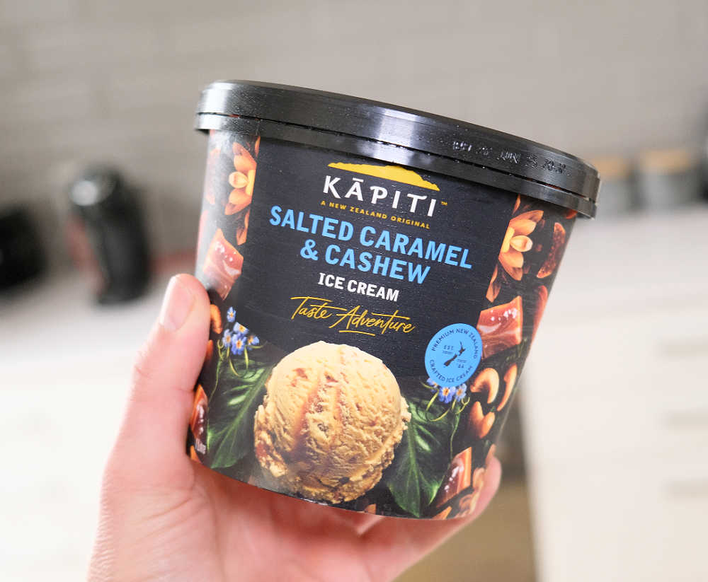 A hand holding a tub of Kapiti Salted Caramel and Cashew Ice Cream.
