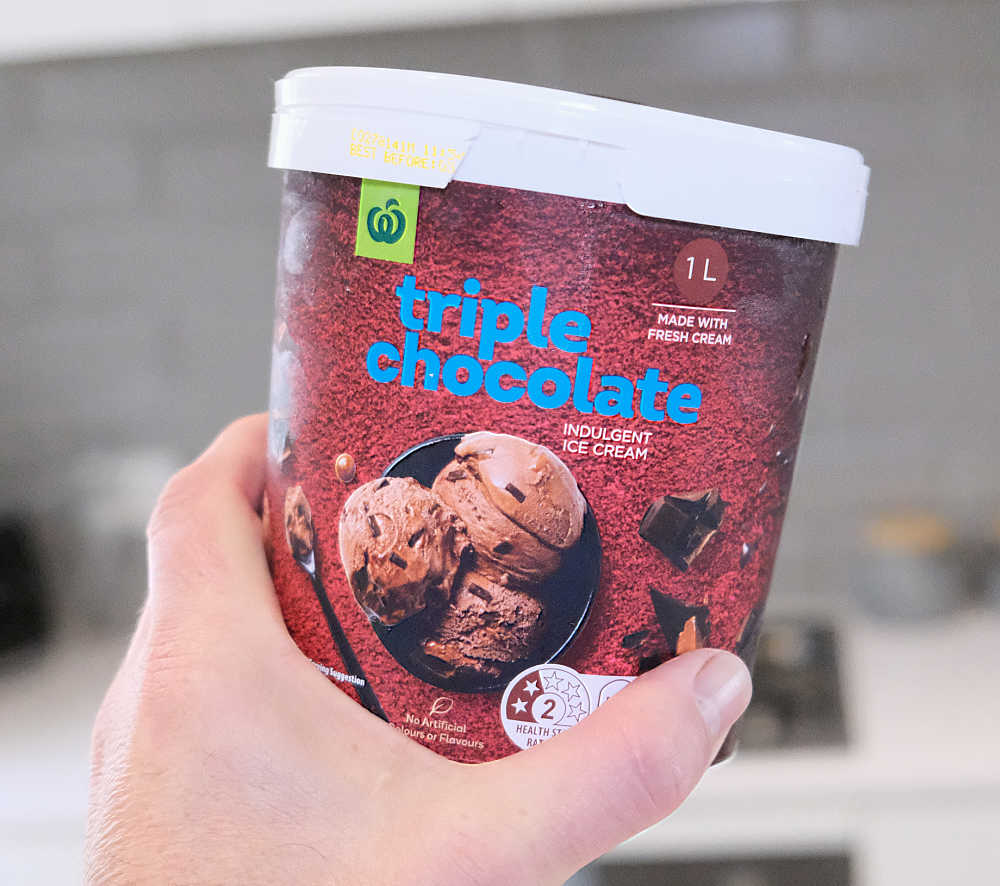 A hand holding a container of Triple Chocolate Indulgent Ice Cream by Woolworths.