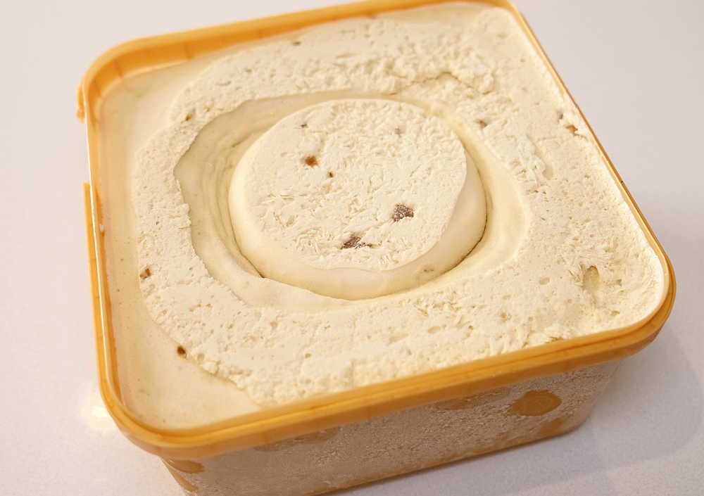 An angled top-down view of an unscooped container of Much Moore Salted Caramel 2L.