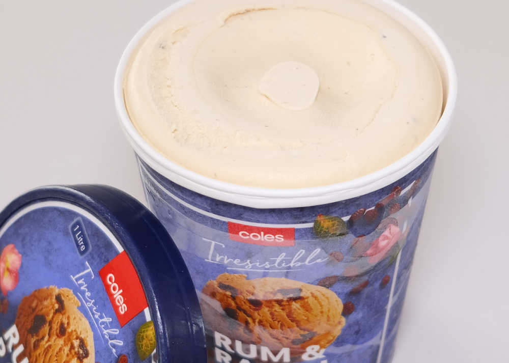 An opened container of Coles Irresistible Rum Raisin Ice Cream with the lid leaning against the side.