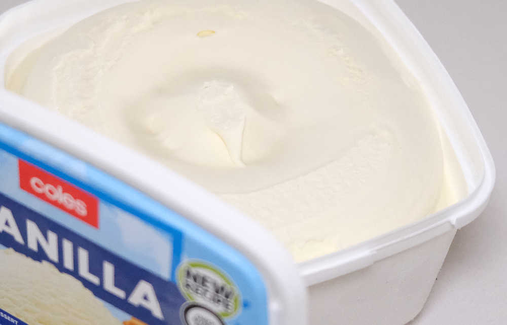 An open container of Coles Vanilla Ice Cream with the lid leaning against the side.