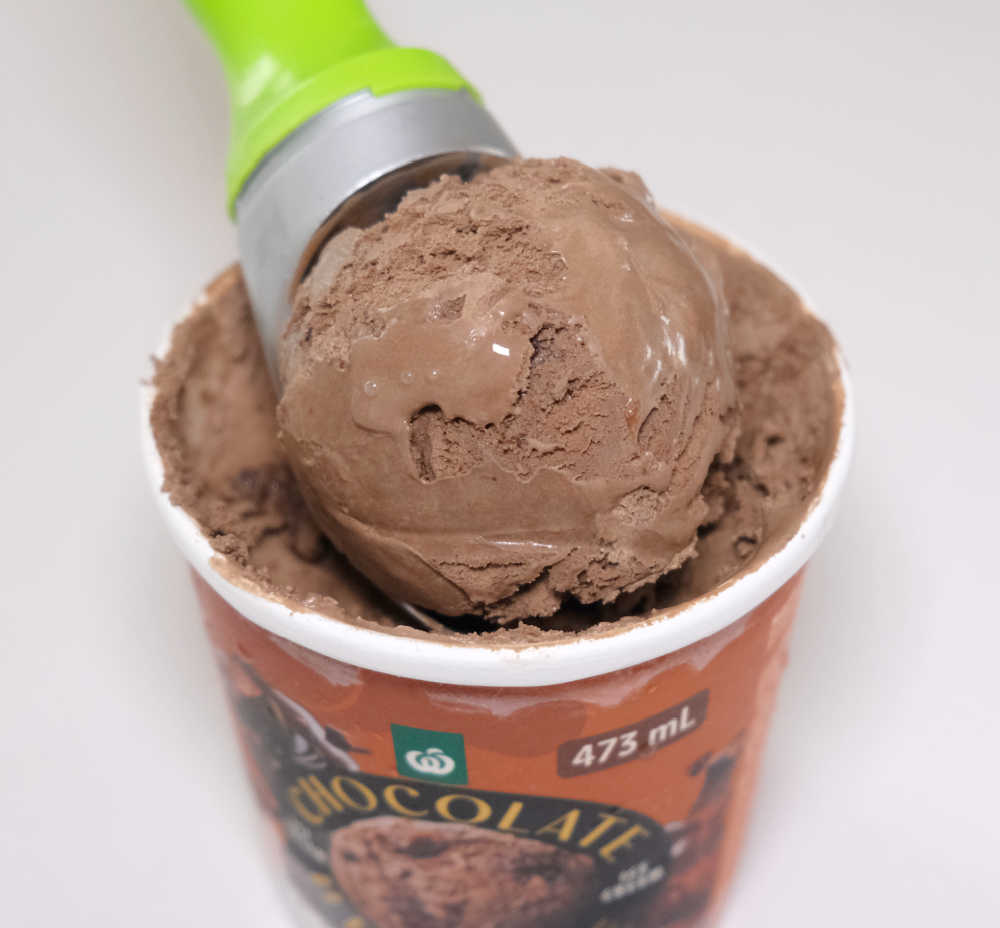 A scoop of chocolate brownie ice cream sitting on the open container.