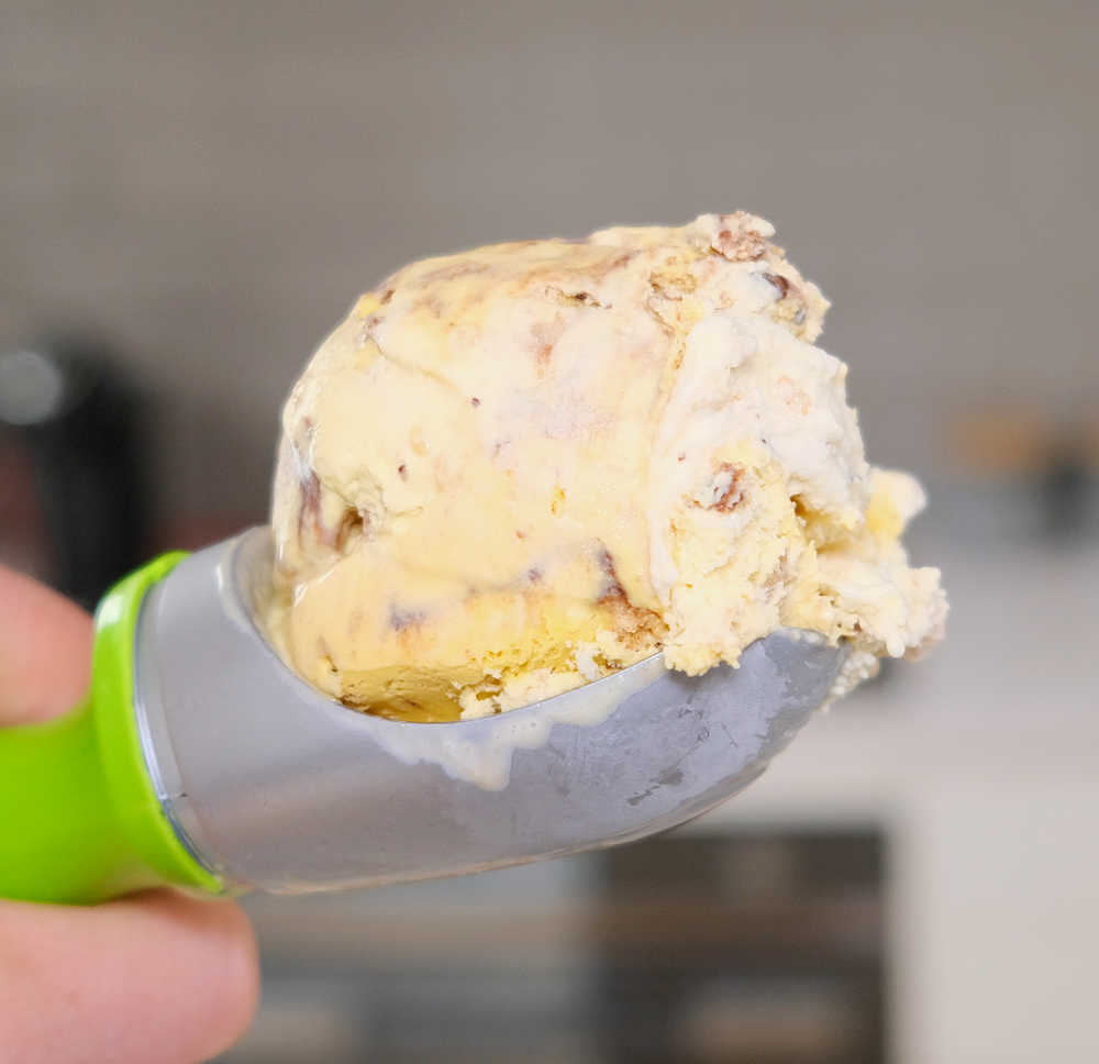 A close-up shot of a scoop of Connoisseur Choc-Chip Cookie Ice Cream with a blurred kitchen in the background.