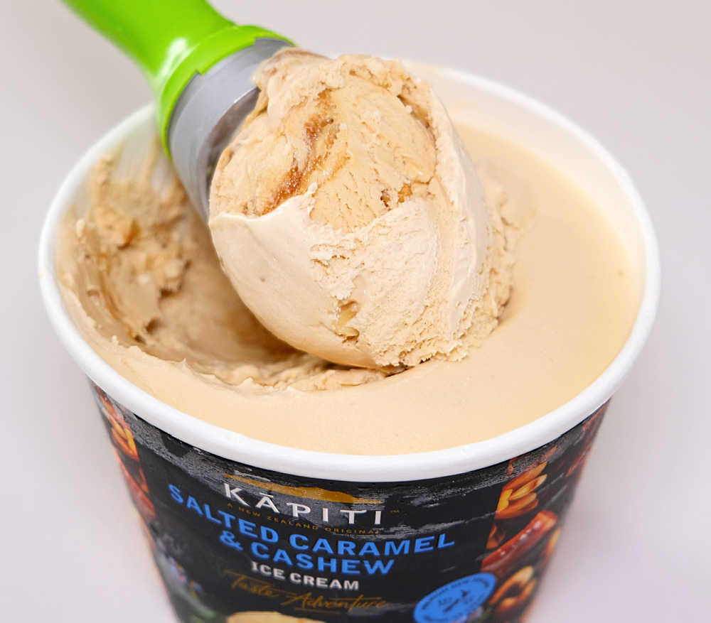 A scoop of Salted Caramel and Cashew Ice Cream resting on the top of the tub.