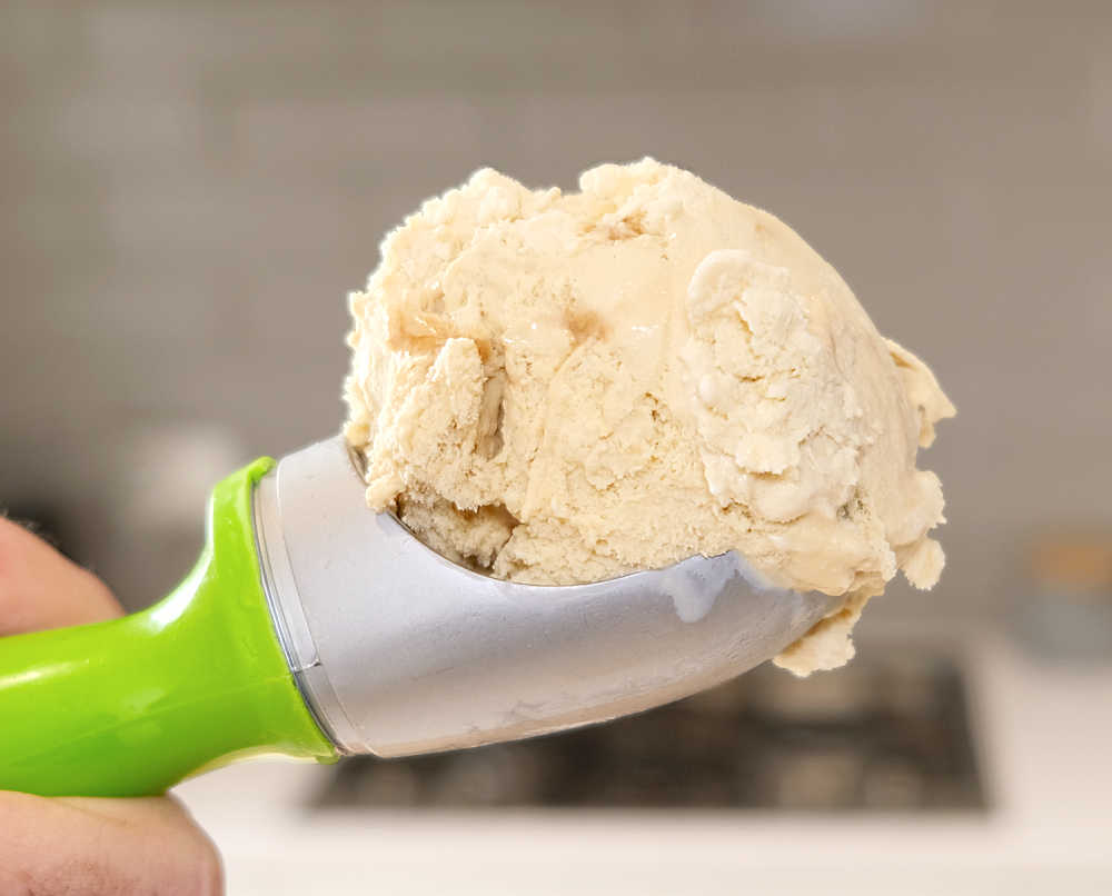 A macro image of a scoop of Much Moore Salted Caramel Ice Cream with a blurred kitchen in the background.