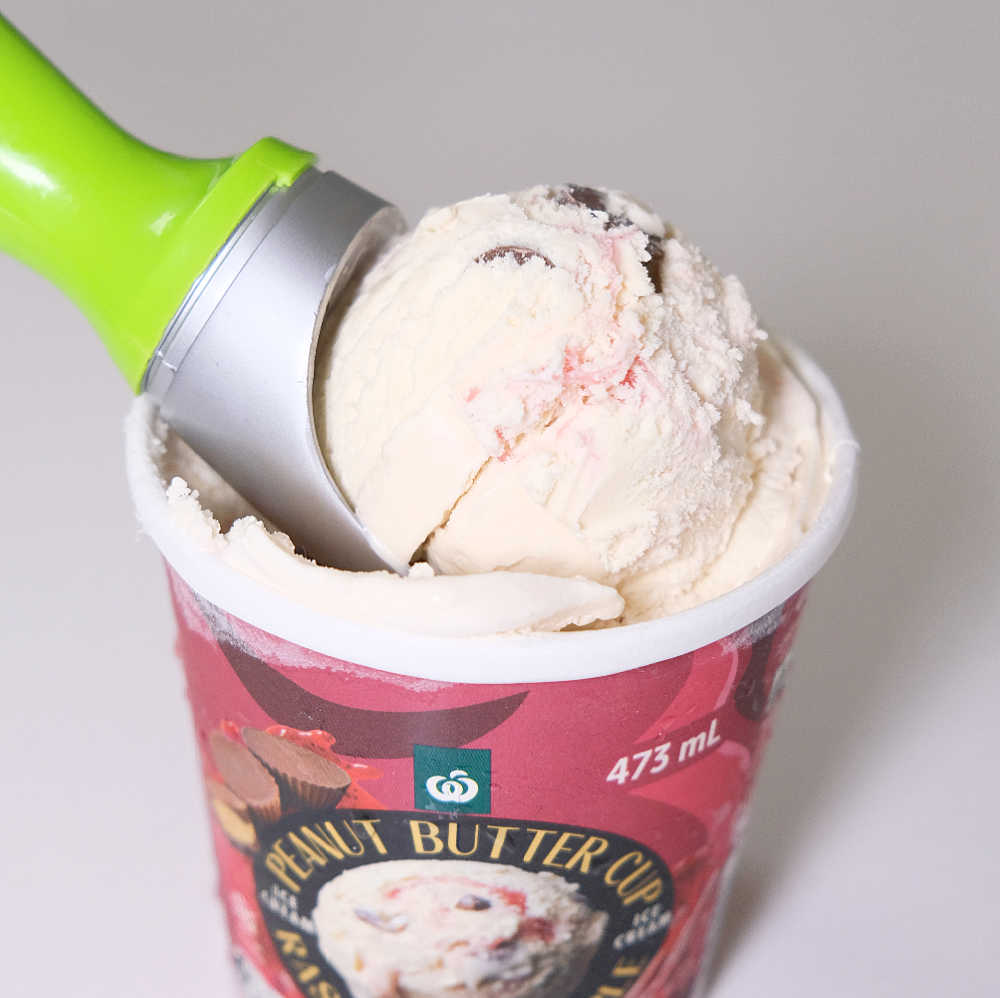 Closeup of a scoop of Woolworths Peanut Butter Cup and Raspberry Ripple Ice Cream resting on the top of the tub.