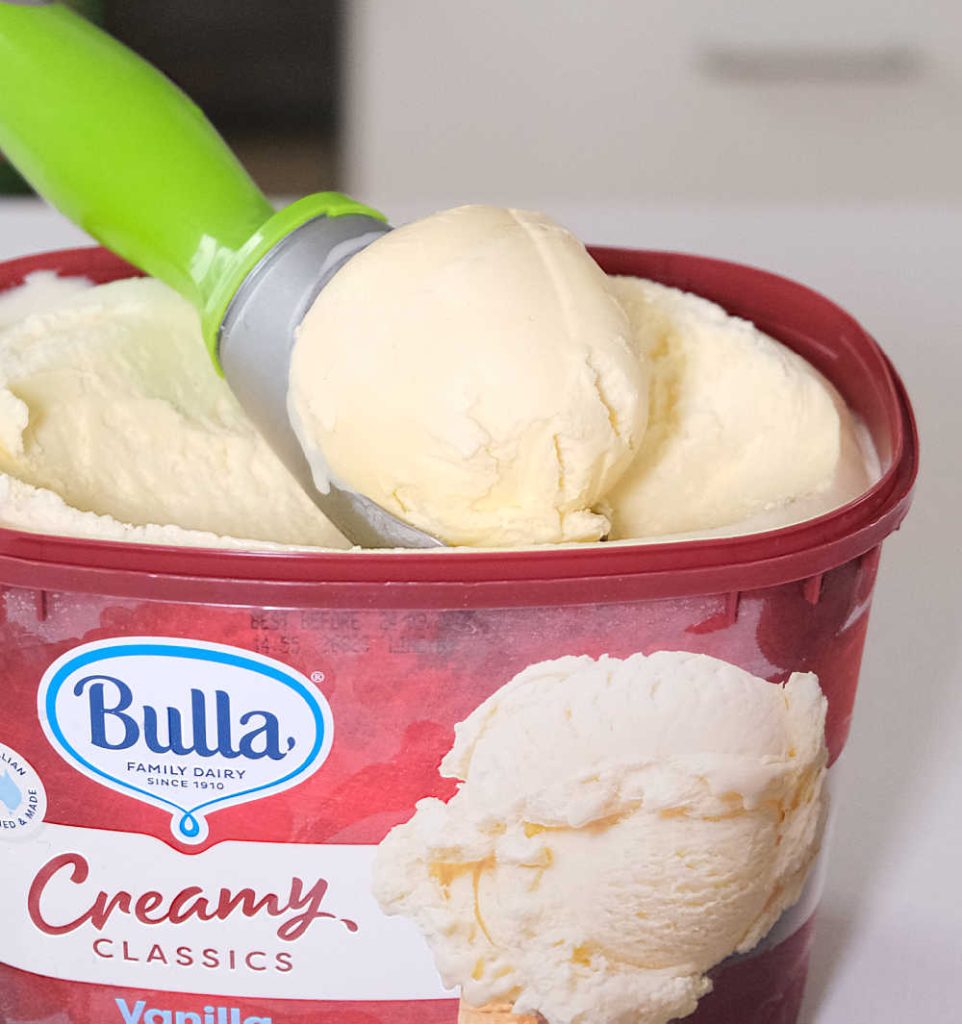 Closeup of a scoop of ice cream resting on the Bulla Creamy Classics Vanilla container.